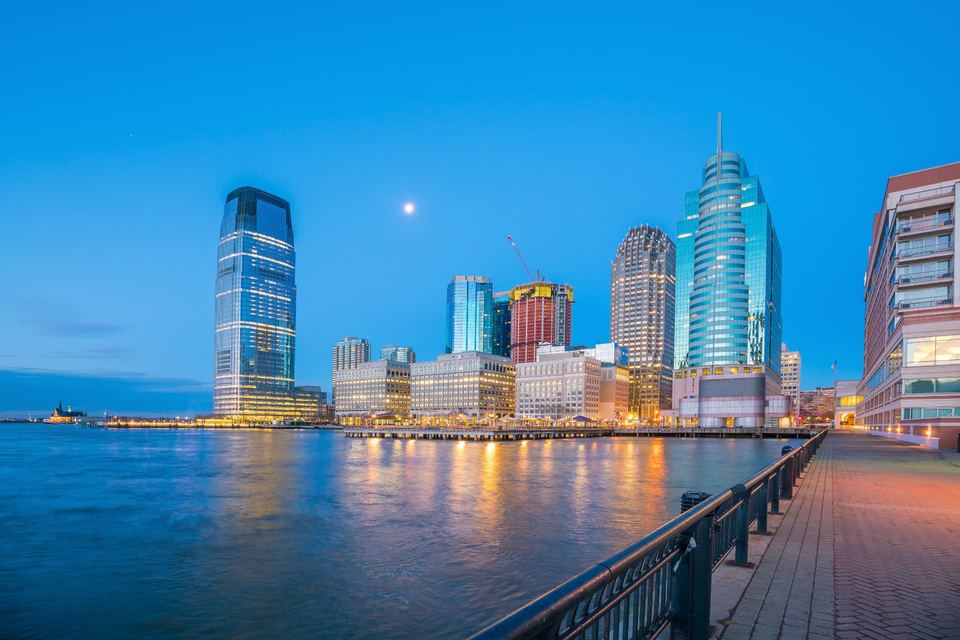 Downtown Jersey City skyline at night with the Hudson River and Lower Manhattan in the distance